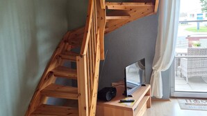 A wooden staircase leading to a lofted area with a flat-screen TV and a speaker on a wooden console. - Vacation home Boddenblick (Barth)
