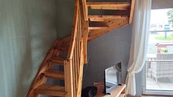 Eine Holztreppe führt zu einer erhöhten Wohnfläche mit einem Flachbildfernseher und einem Lautsprecher auf einer Holzkonsole.