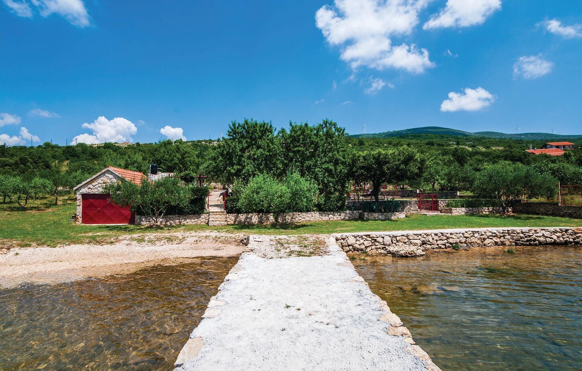 A stone pathway leading to a red building, surrounded by greenery and a body of water.