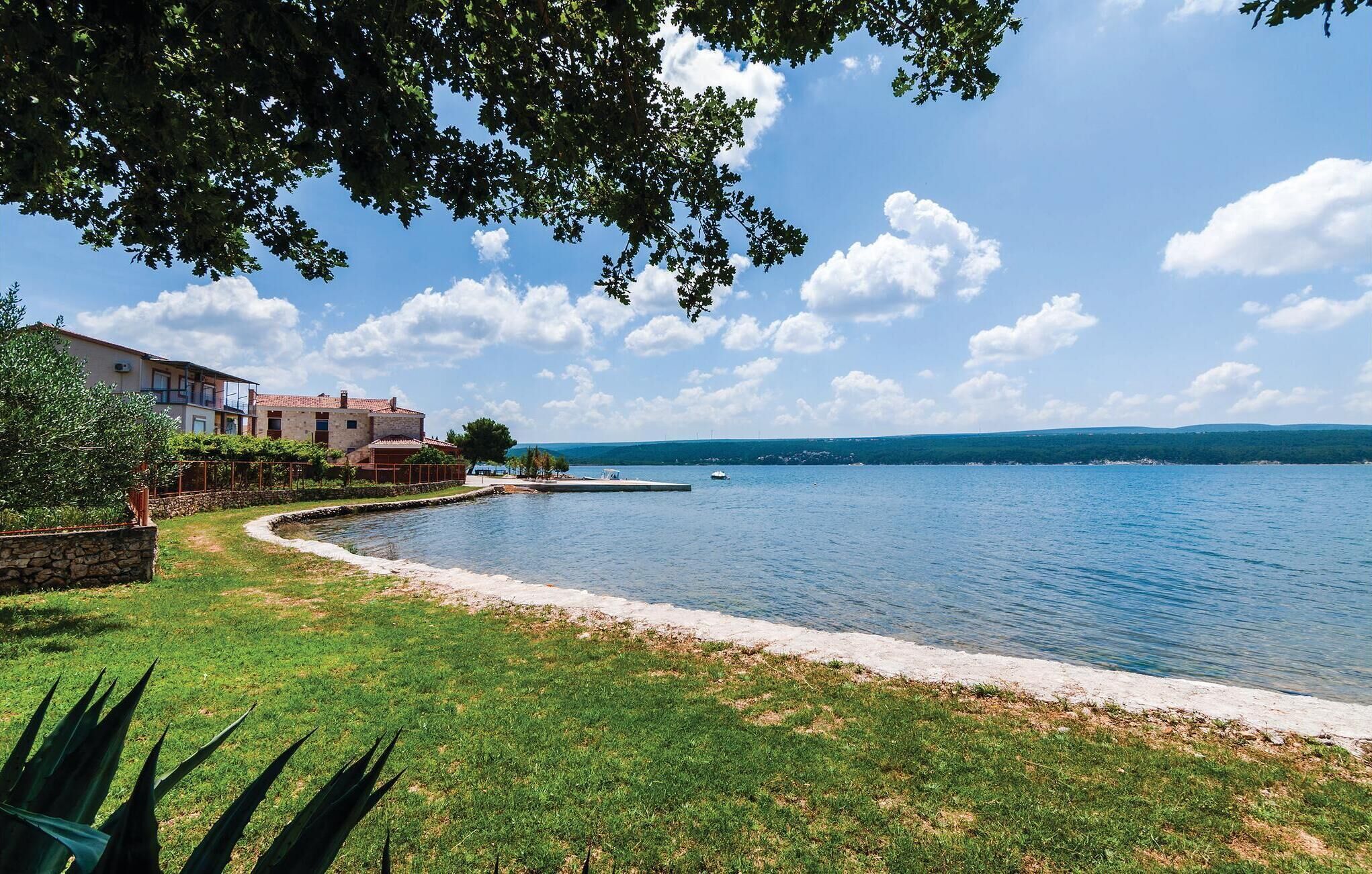 Una propiedad junto al lago con un muro de piedra, un área cubierta de césped y un edificio con balcón con vista al agua.