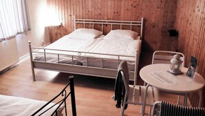 Un dormitorio con estructura de cama metálica, una mesita redonda con una silla y suelo de madera.