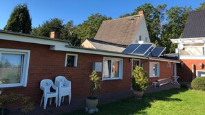 Una casa de ladrillo con paneles solares, sillas de plástico blanco y una planta en maceta.