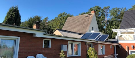 A brick house with solar panels, white plastic chairs, and a potted plant.