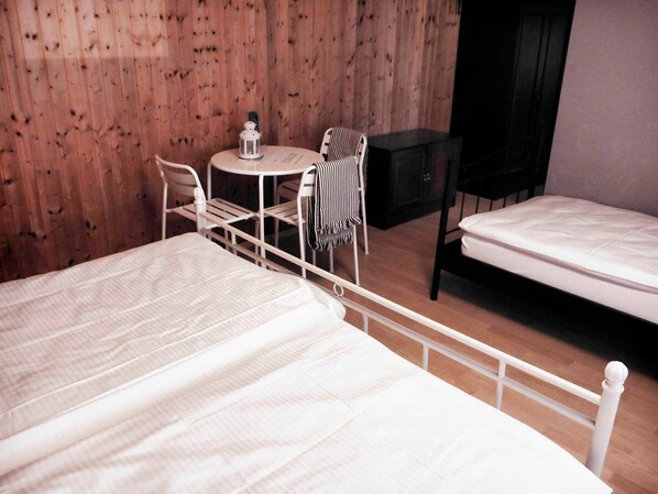 Une chambre avec deux lits, une petite table ronde avec une chaise, un meuble noir et un mur en bois.