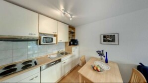 Une cuisine moderne avec des meubles blancs, un four à micro-ondes et une cuisinière. On y trouve une table à manger avec des chaises et un vase rempli de fleurs.