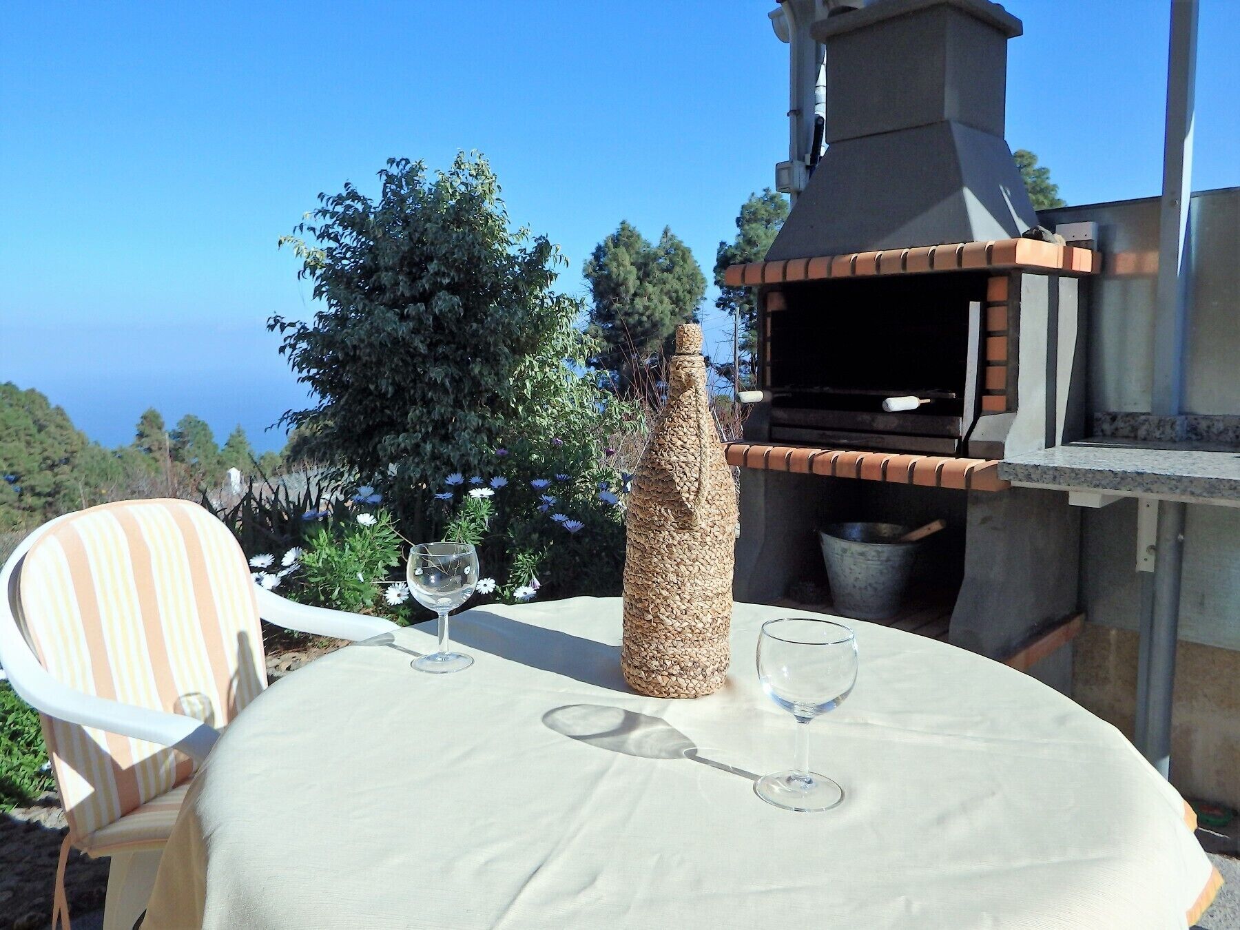 An outdoor dining area with a table, chairs, a wine glass, and a stone bottle.