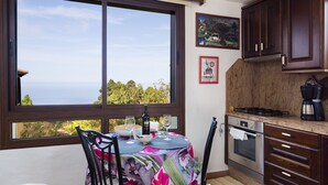 Een keuken met een groot raam, een eettafel met stoelen en uitzicht op zee.