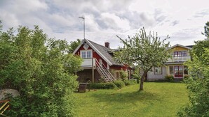 A residential area with two houses, one with a red exterior and a stone foundation, and another with a yellow exterior. There is a grassy yard with a small tree and a stone wall. - Nice home in Löttorp with WiFi (Löttorp)