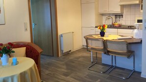 A compact kitchen with a dining area, featuring a table with chairs, a vase of flowers, and a hanging light fixture.