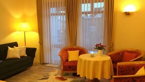A cozy room with a green sofa, a floral armchair, a small table with a vase of flowers, and a lamp.