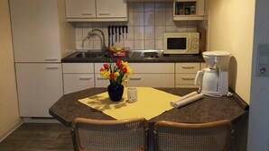 A compact kitchen with white cabinets, a microwave, a coffee maker, and a dining table with two chairs.
