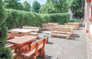An outdoor seating area with wooden tables and benches, surrounded by hedges and a brick pathway. - Nice home in Petershagen OT Frille (Petershagen OT Frille)