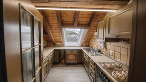 A narrow kitchen with wooden beams, a skylight, and a view of the outside.