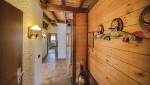 A wooden interior hallway with a tiled floor, a door with a light switch, and wall-mounted light fixtures.