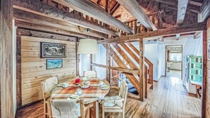 A rustic wooden dining area with a table set for four, a staircase, and a view of a bedroom with a green cabinet.
