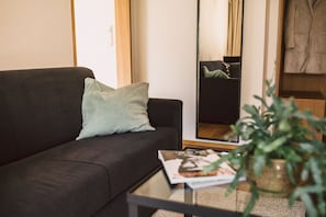 A living room with a dark sofa, a light green pillow, a magazine on a small table, and a large mirror reflecting the room.