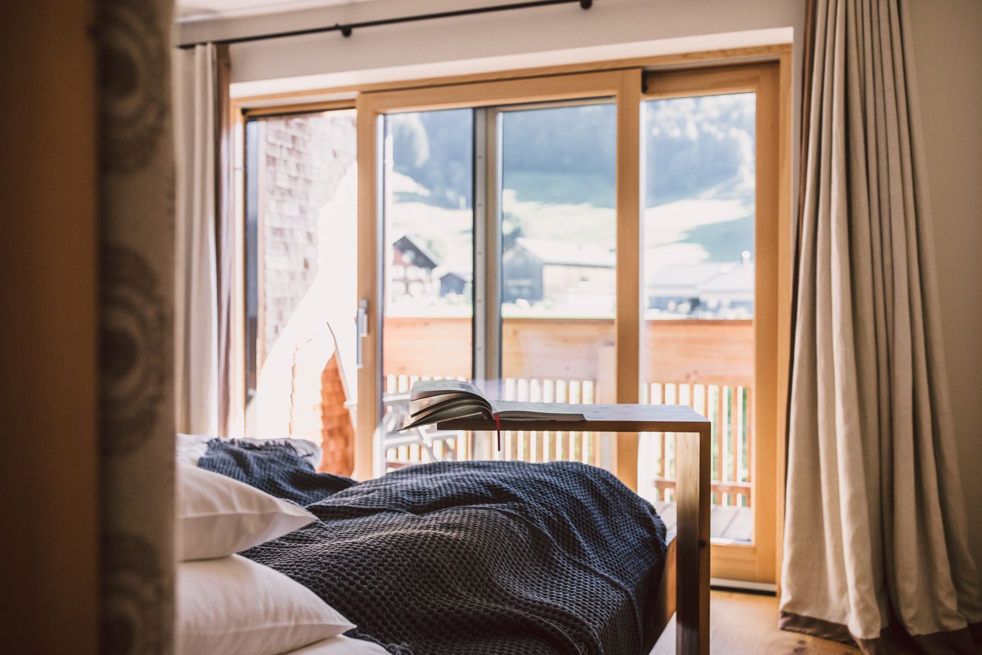 Un dormitorio con cama, una mesa con libros, una ventana que ofrece vistas a un paisaje nevado y cortinas.