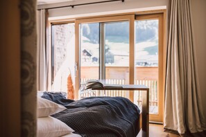 Een slaapkamer met een bed, een tafel met boeken, een raam met uitzicht op een besneeuwd landschap en gordijnen.