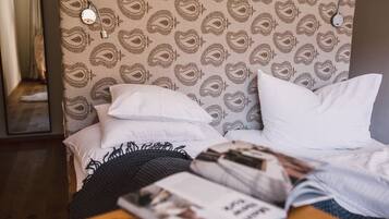 A bed with white pillows and a patterned headboard, a wooden nightstand with a magazine, and a mirror on the wall.