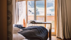 Une chambre à coucher avec un lit, une table avec des livres, une fenêtre donnant sur un paysage enneigé et des rideaux.