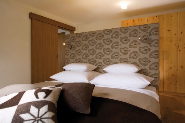 A bedroom with a bed, pillows, a blanket, wooden walls, and a patterned wallpaper.