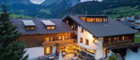 A hotel with a terrace, outdoor seating, and a mountain backdrop.