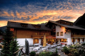 A hotel with outdoor seating, a stone facade, and a mountain backdrop.