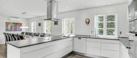 Una cocina moderna con armarios blancos, una isla grande y un comedor con mesa y sillas.