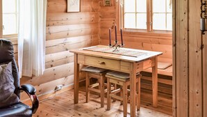 Interior d'una cabana de fusta amb escriptori, cadira i finestra amb cortines.