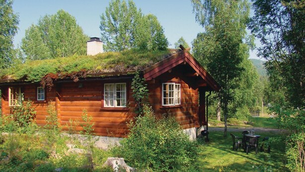 Una cabana de fusta amb teulada verda, envoltada d'arbres i una zona enjardinada amb mobiliari exterior.