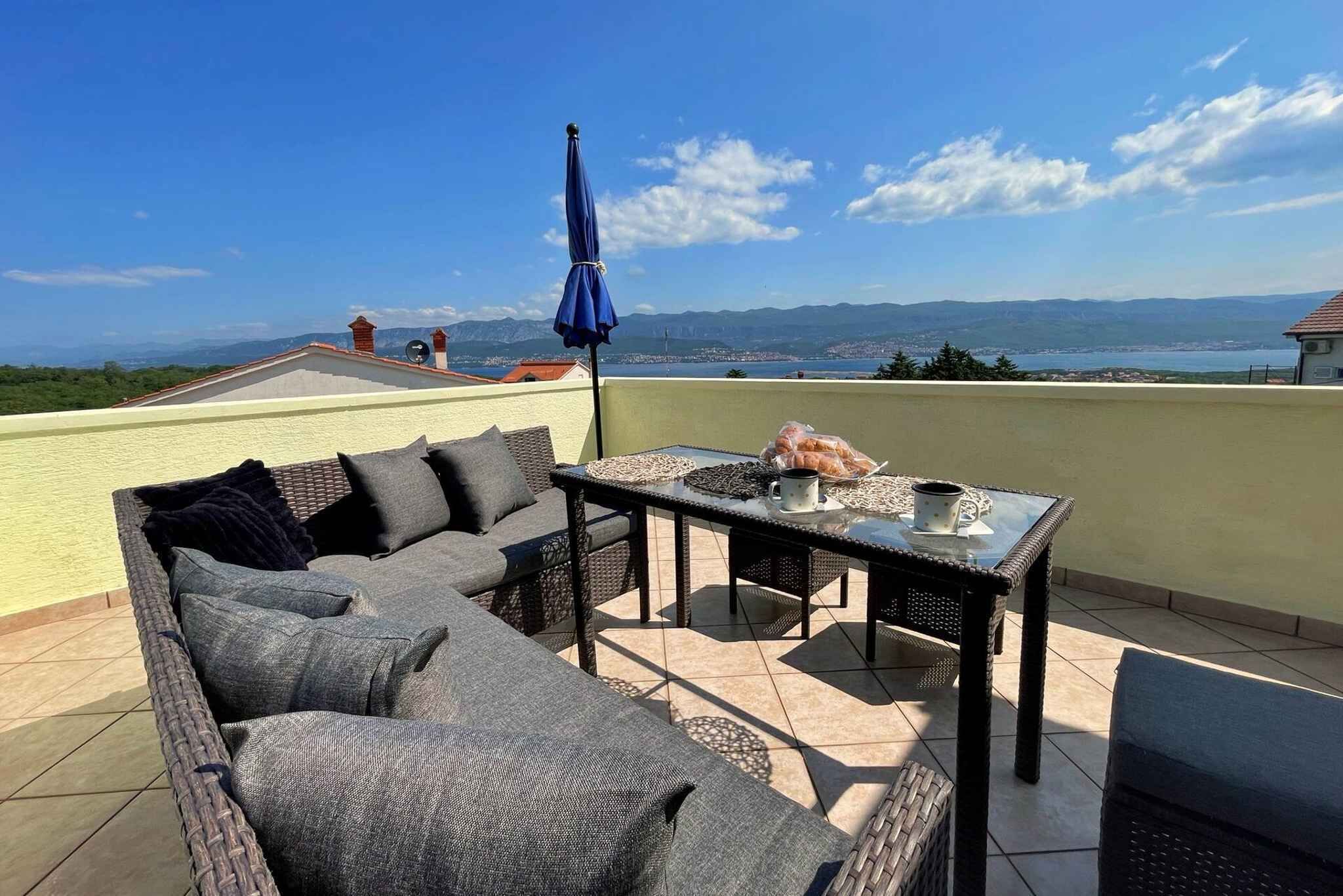 A rooftop terrace with a sofa, table, and umbrella, overlooking a scenic landscape.