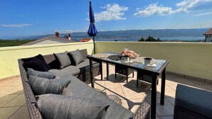 Eine Dachterrasse mit Sofa, Tisch und Sonnenschirm, mit Blick auf eine reizvolle Landschaft.
