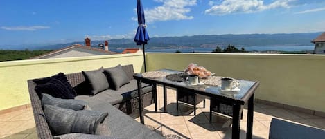 A rooftop terrace with a sofa, table, and umbrella, overlooking a scenic landscape.
