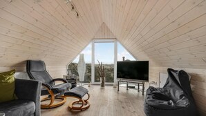 Un espacio habitable acogedor y de planta abierta, con techo alto y ventanas amplias, que incluye un sofá de cuero negro, un sillón inflable negro y un televisor de pantalla plana.