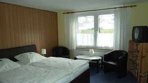 Ein Hotelzimmer mit Bett, Schreibtisch, Stuhl, Fernseher und einem fensterbepflanzten Fenster.