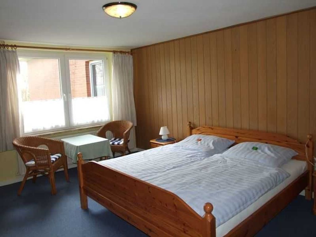 Una habitación con una cama de madera, una mesita, una silla y una ventana con cortinas.