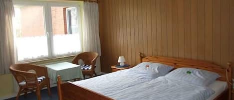 A room with a wooden bed, a small table, a chair, and a window with curtains.