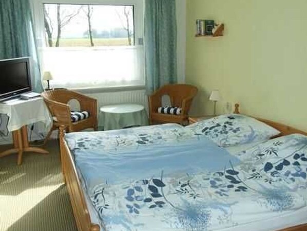 A bedroom with a bed, a chair, a small table, a television, and a window with curtains.