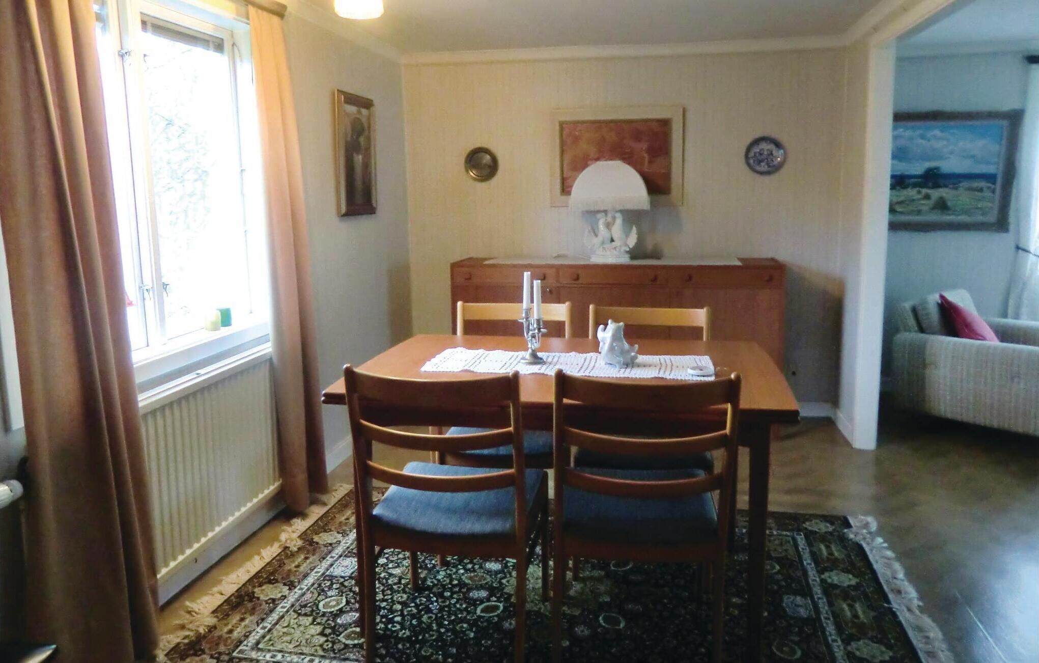 Un comedor con una mesa de madera, cuatro sillas, una lámpara y un cuadro en la pared.