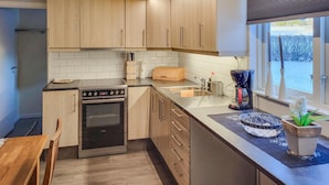 A modern kitchen with wooden cabinets, a built-in oven, a coffee maker, and a window with a view of a snowy landscape. - 3 bedroom lovely home in Vetlanda (Vetlanda)