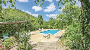 Zona de piscina con sillones de descanso y una pérgola, rodeada de vegetación exuberante y colinas.