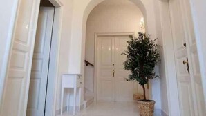 Een gang met witte deuren, een kroonluchter en een potplant.