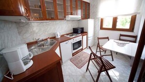 Een kleine keuken met houten kastjes, een inbouwmagnetron, een koffiezetapparaat en een eethoek met een tafel en stoelen.