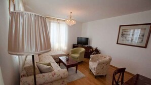 Een woonkamer met een bank, fauteuils, een salontafel, een televisie en een kroonluchter.