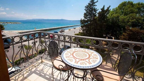 Een balkon met een ronde tafel en stoelen, met uitzicht op een kustgebied met een weg en begroeiing.