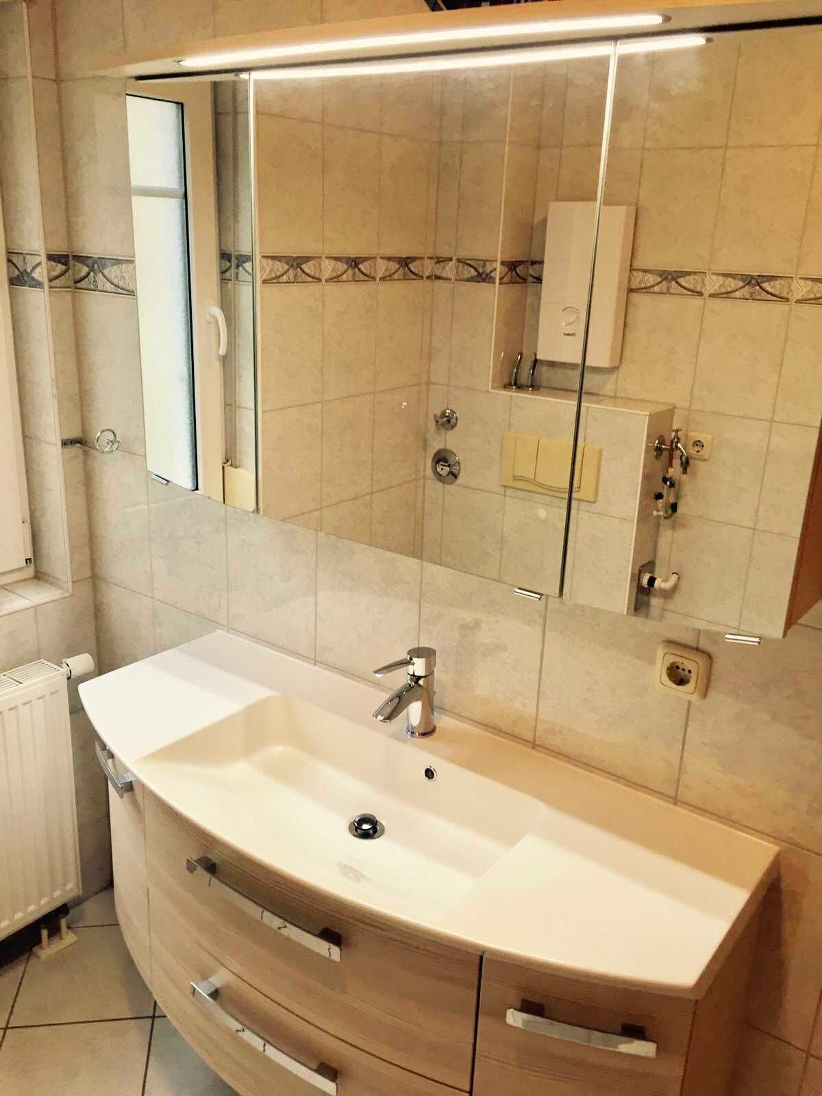 A modern bathroom with a curved sink, a large mirror, and a shower area.