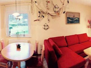 Um quarto aconchegante com um sofá vermelho, uma mesa de jantar redonda e uma janela com vista para um jardim.