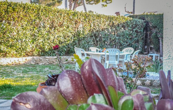 Un jardin avec une table et des chaises, entouré de différentes plantes et d’un mur de pierre.