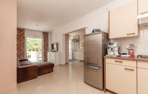 A modern kitchen with a refrigerator, coffee maker, and a dining area with a sofa and a television. - 2 bedroom beach front apartment in Pirovac (Pirovac)
