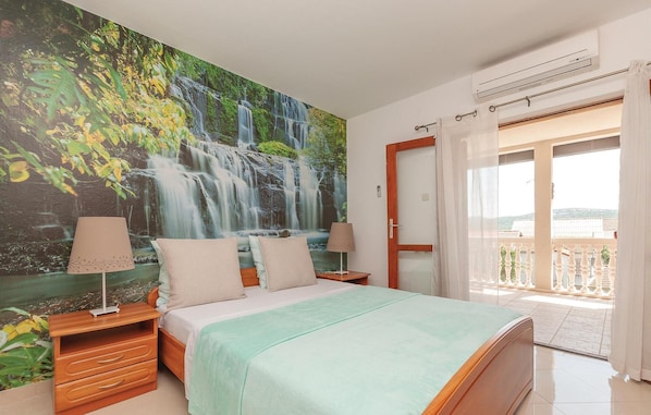 A bedroom with a large waterfall mural, a bed with a green bedspread, wooden nightstands, two lamps, and a sliding glass door leading to a balcony. - 2 bedroom beach front apartment in Pirovac (Pirovac)
